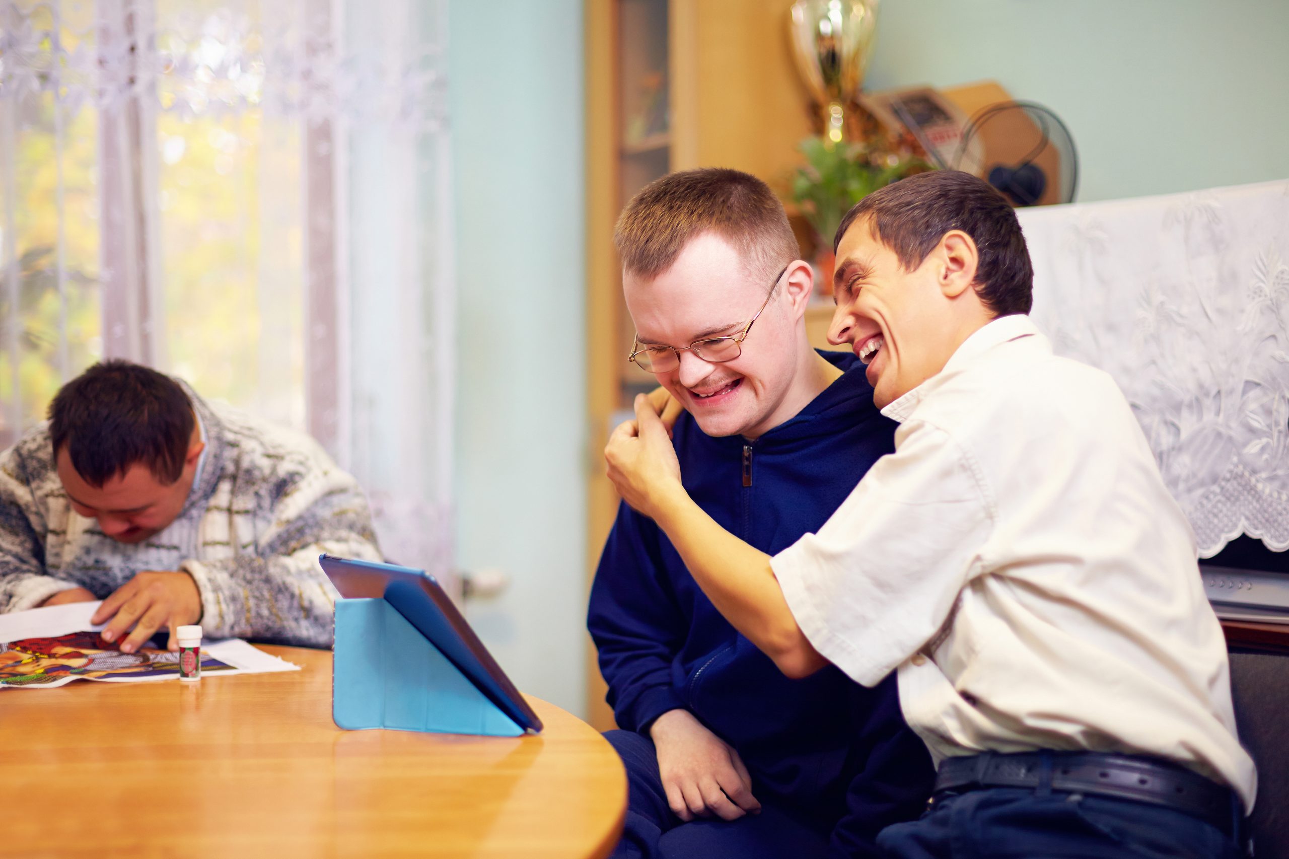 Zwei Männer mit einer Behinderung schauen zusammen auf ein Tablet und sind glücklich.